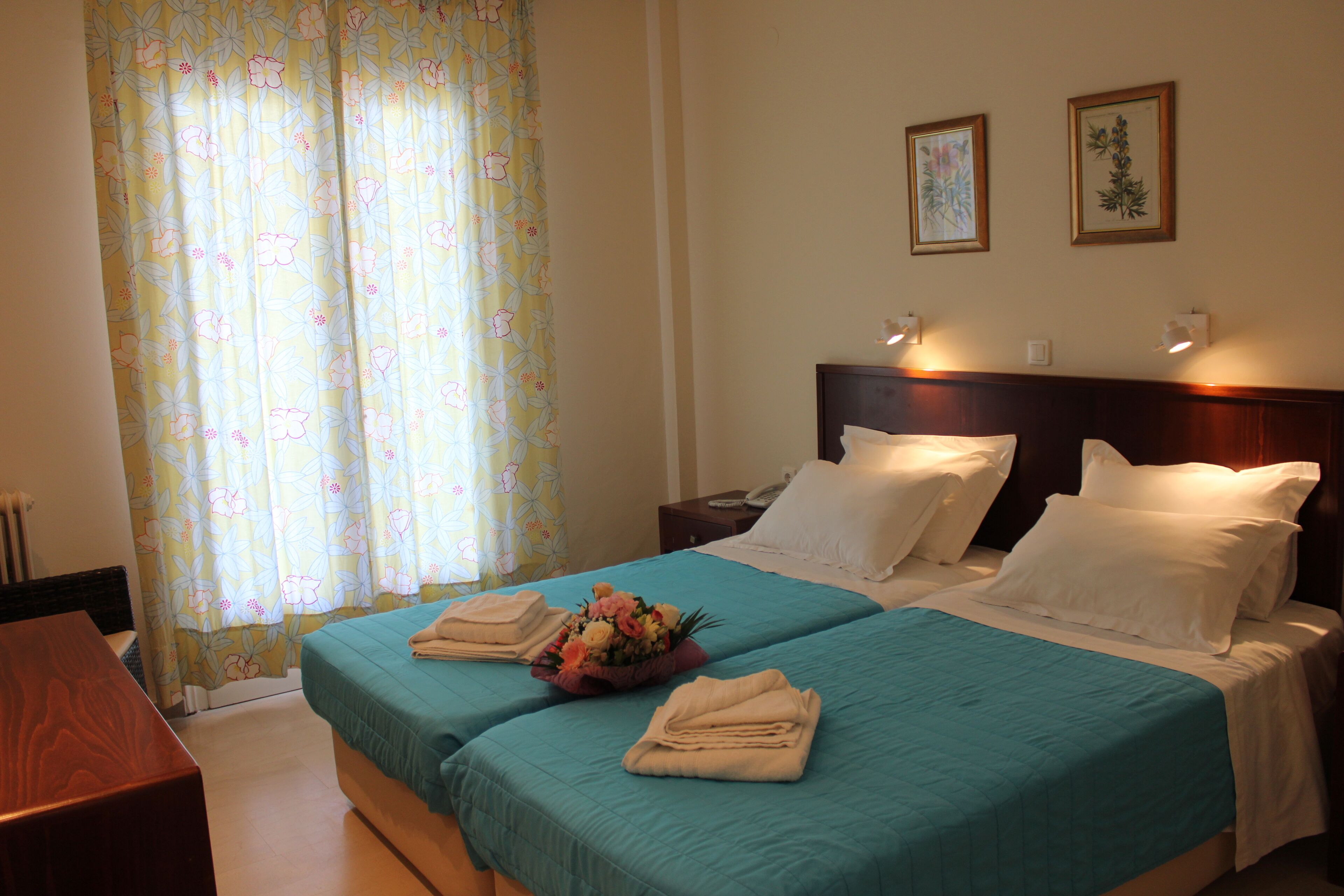 A hotel room with two beds, floral curtains, and a nightstand with a lamp.
