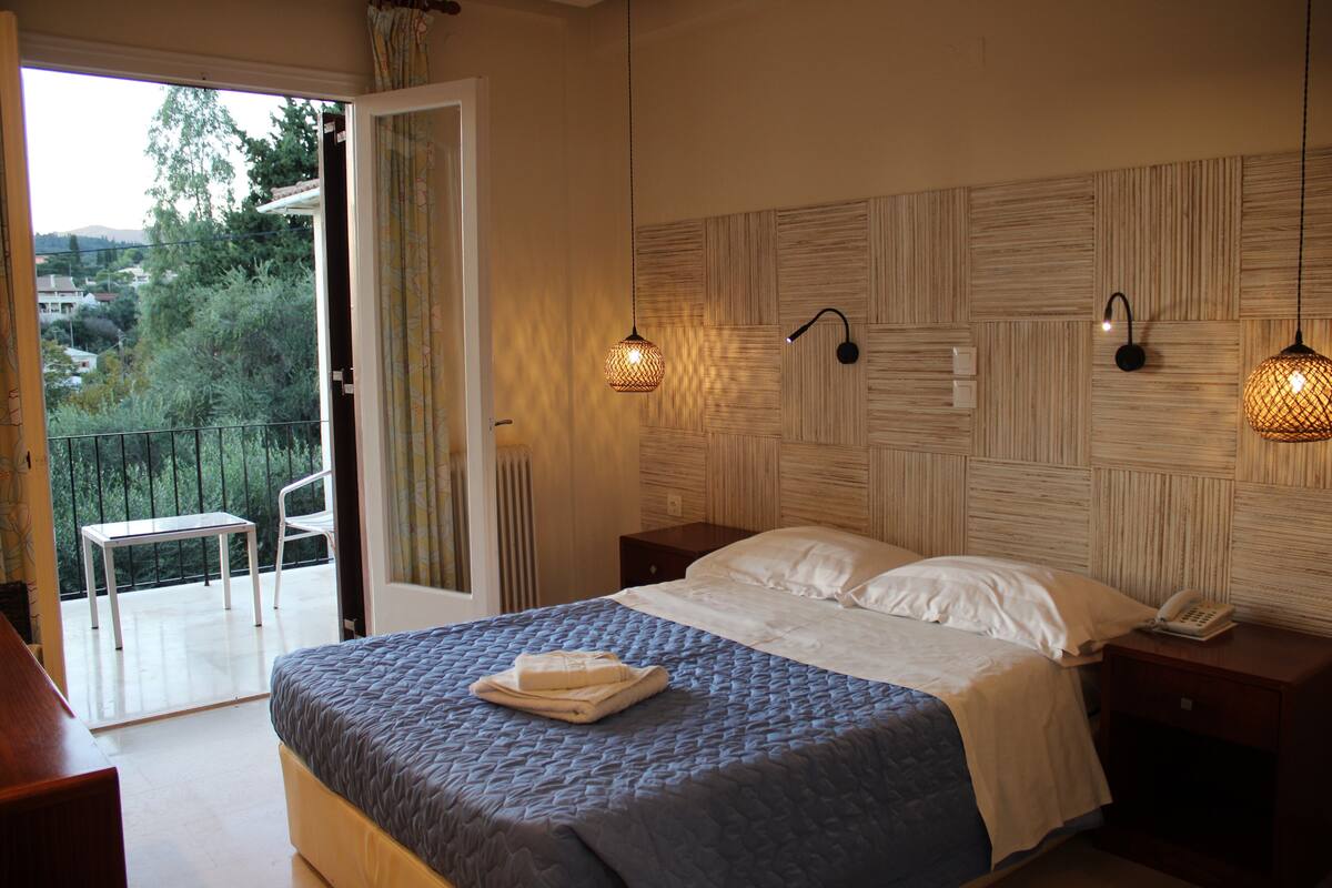 A bedroom with a bed, bedside tables, a telephone, and a view of the outdoors.