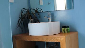 A bathroom with a white sink, a mirror above it, and a wooden cabinet below. There is a plant in a pot on the sink and a towel folded on the cabinet shelf.