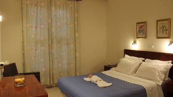 A hotel room with a bed, a wooden table, a chair, a desk, a telephone, and a curtain with a floral pattern.