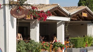 Restaurante com mesas ao ar livre, placa indicando que é um café e placa de proibido estacionar na calçada.