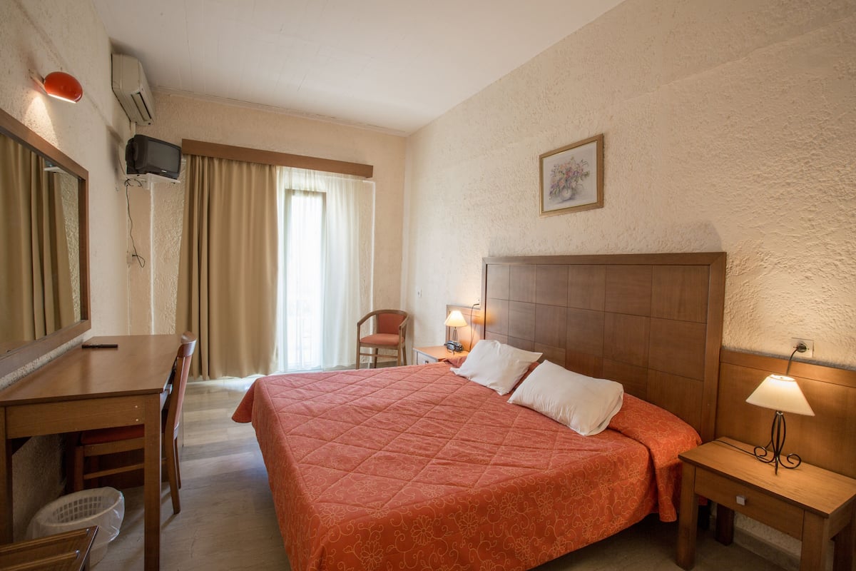 Una habitación de hotel con una cama grande, un escritorio, una silla, un televisor montado en la pared y una ventana con cortinas.