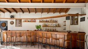 Uma área de bar com banquetas de madeira, estantes com garrafas e um alvo de dardo na parede.