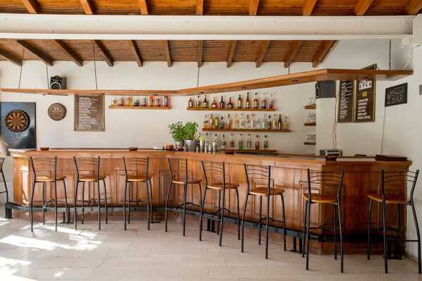 A bar area with wooden bar stools, shelves with bottles, and a dartboard on the wall. - Popi Star (Corfu)