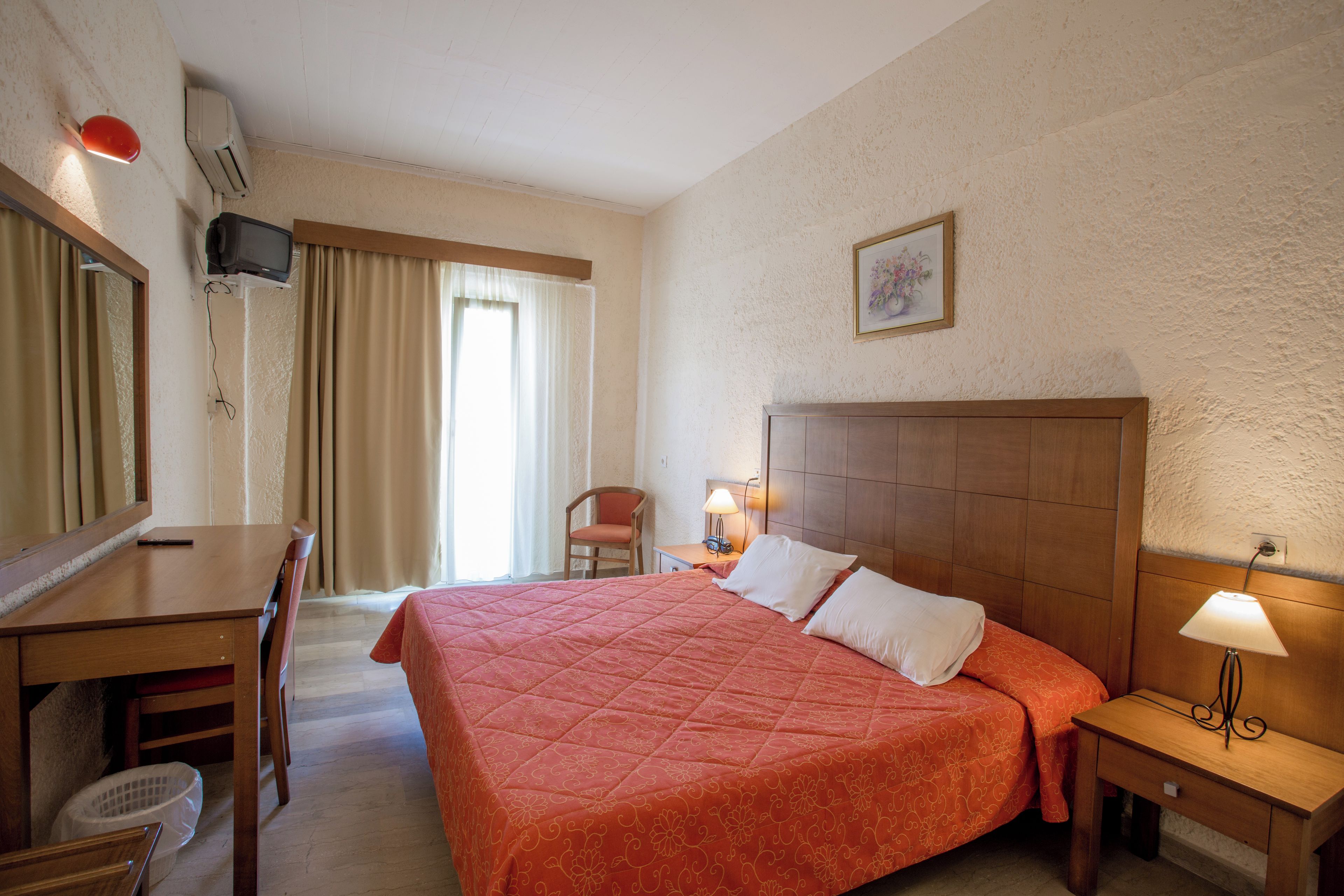Habitación de hotel con cama, escritorio, silla, televisor y ventana con cortinas.