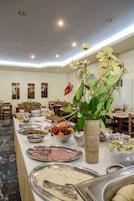 Montaje de bufé con diversos alimentos, un florero con flores y mesas y sillas para comer.