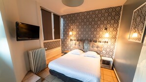 A bedroom with a bed, a TV mounted on the wall, and a patterned wallpaper. - Citotel Furania (Saint-Etienne)