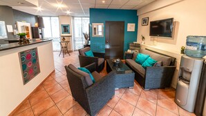 A modern living area with dark wicker furniture, a water dispenser, and a TV mounted on the wall. - Citotel Furania (Saint-Etienne)