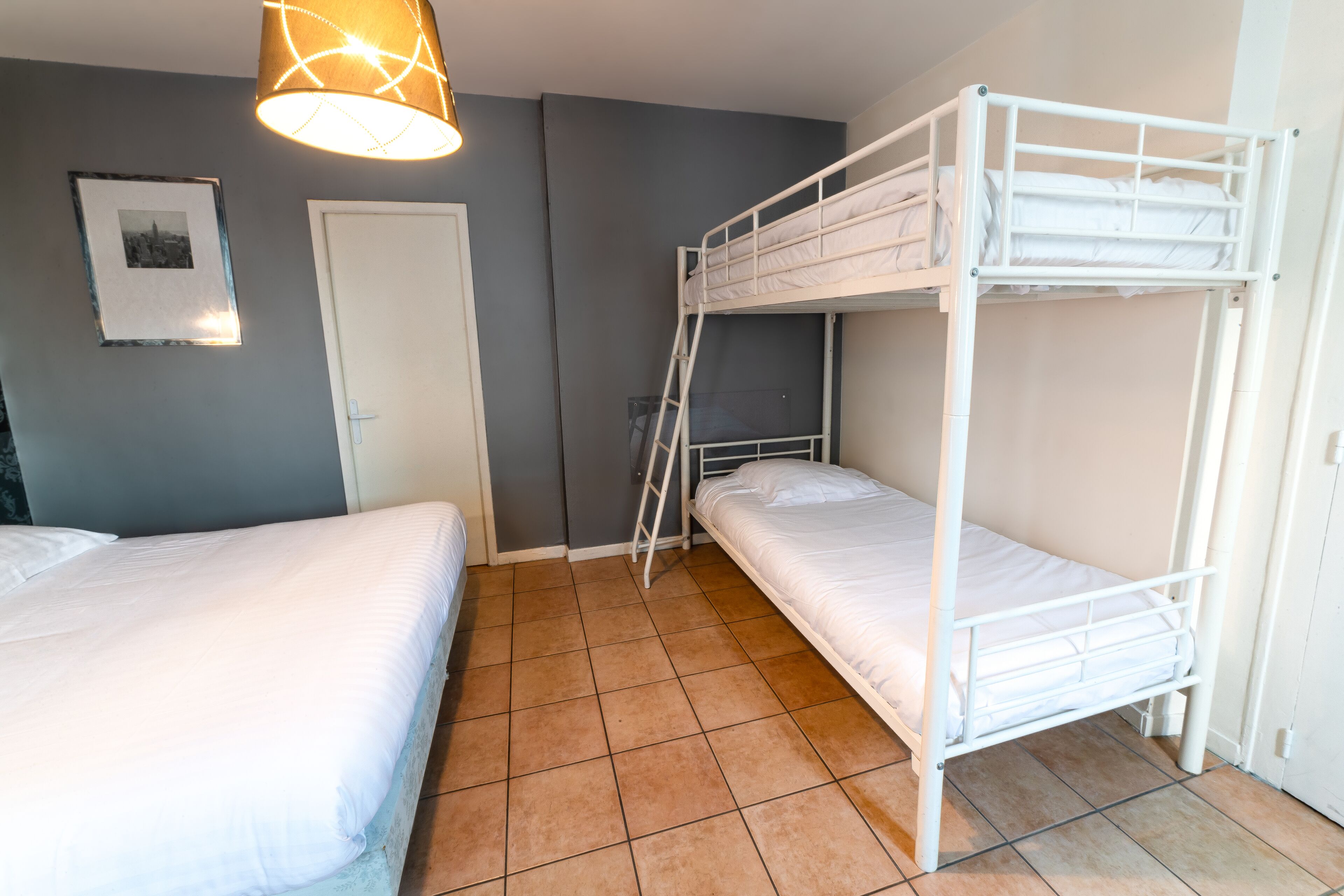 Une chambre avec deux lits simples, un lit superposé, une porte et un tableau accroché au mur.