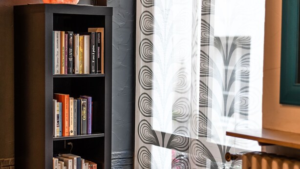 A room with a bookshelf, a table with a decorative bowl, and patterned curtains. - Citotel Furania (Saint-Etienne)