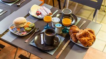 A breakfast setup with a croissant, a sandwich, kiwi slices, and a glass of orange juice on a table.
