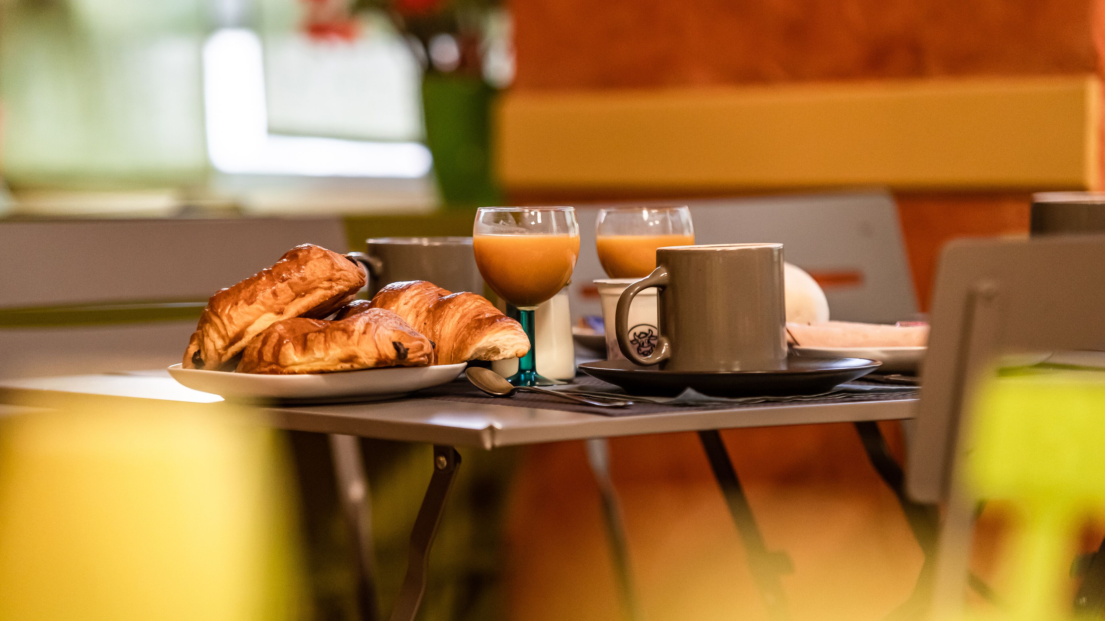 Un desayuno con cruasanes, una taza de café y un vaso de jugo de naranja sobre una mesa.