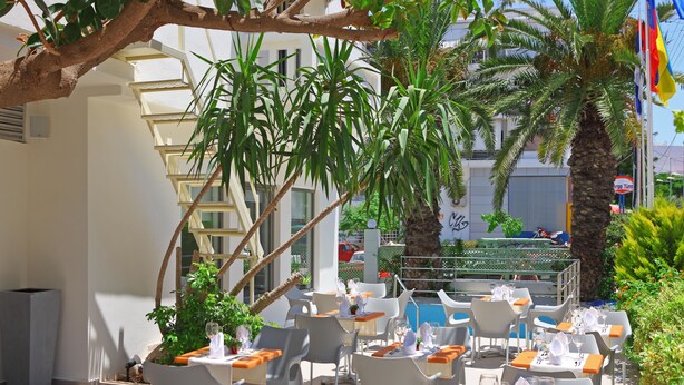 Un café en plein air avec des tables et des chaises blanches, entouré de verdure et de palmiers.