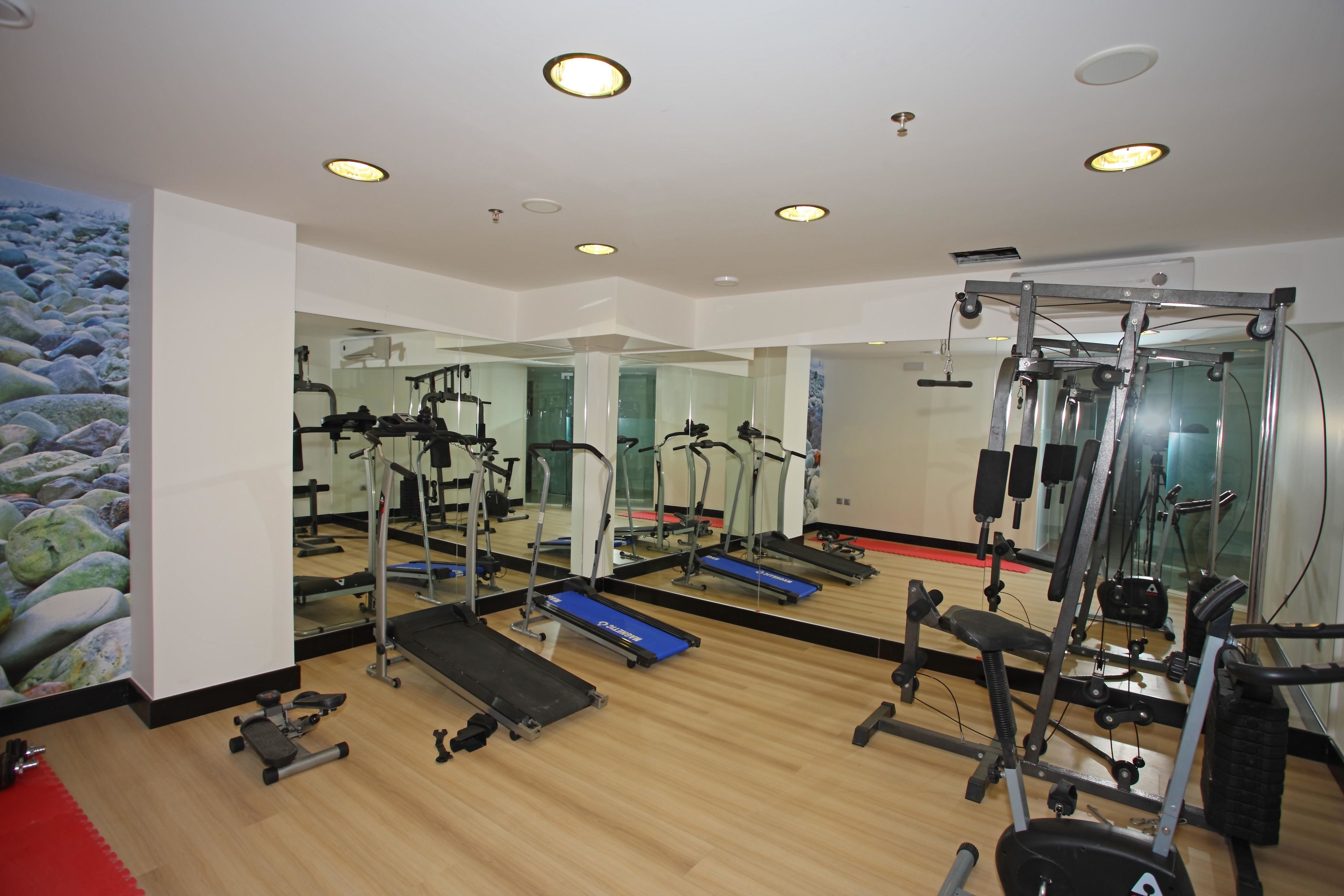 A gym with exercise equipment, mirrors, and wooden flooring.