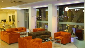 Un hall d’hôtel moderne avec des canapés orange, une table basse et un téléviseur.