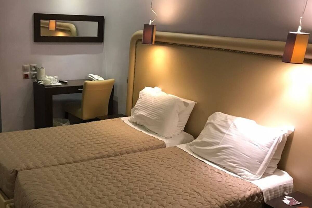 Habitación de hotel con dos camas, un escritorio, una silla y una lámpara de noche.