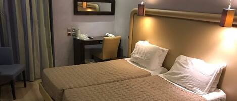 A hotel room with two beds, a desk, a chair, and a bedside lamp.