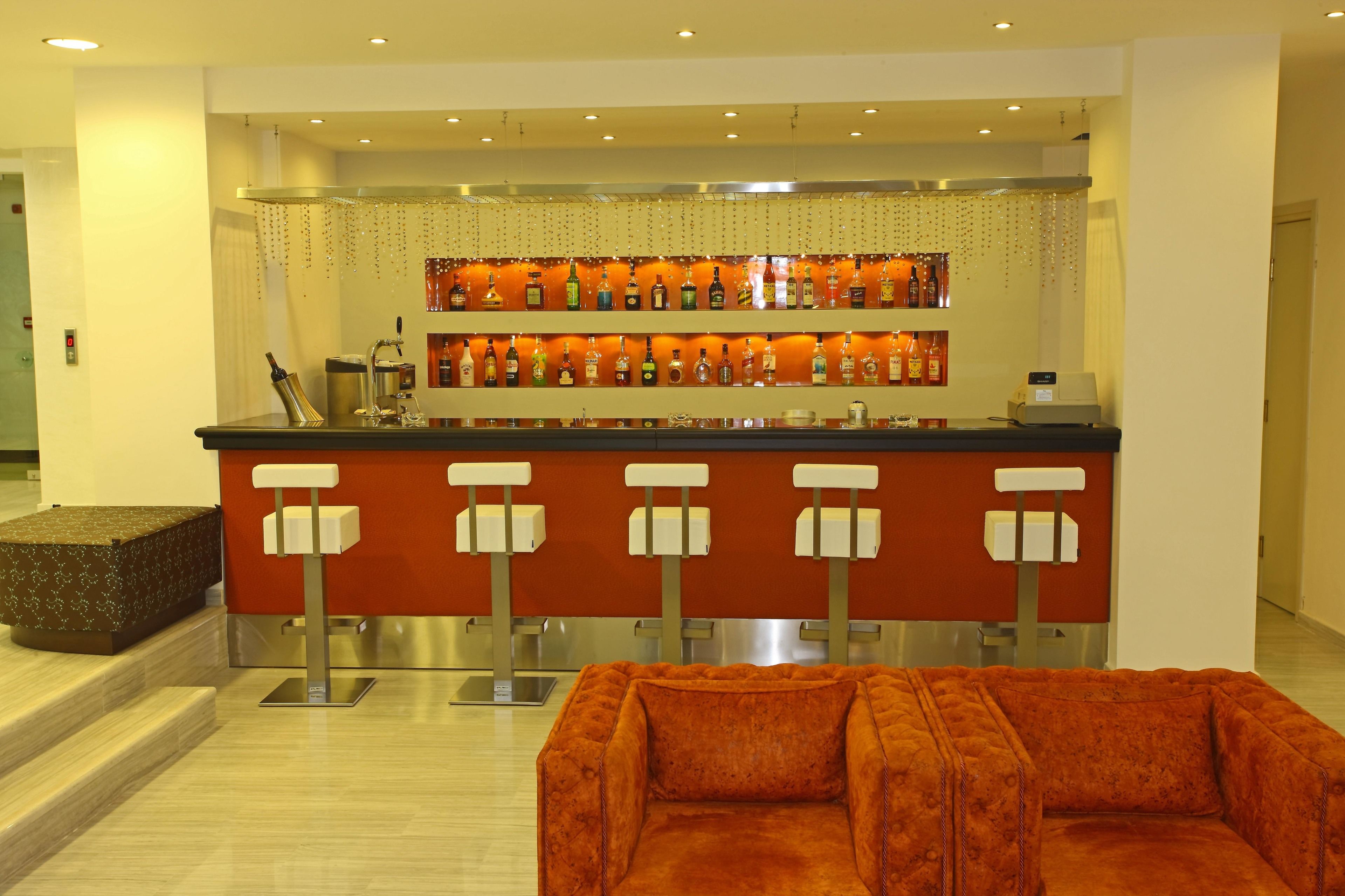A bar area with a counter and multiple stools, a plush orange sofa, and a wall of liquor bottles.