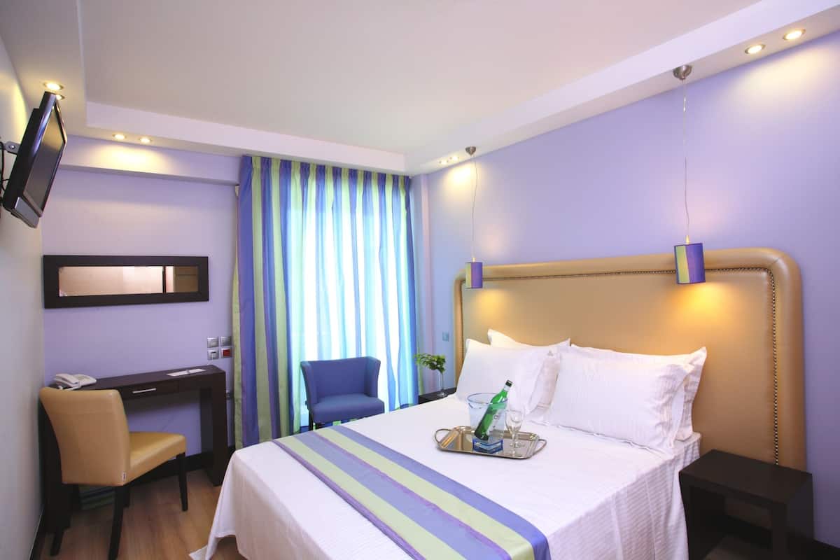 Una habitación de hotel con cama, escritorio, silla, televisor y ventana con cortinas.