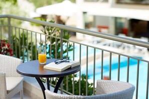 A round table with a book and a glass of orange juice, a wicker chair, and a view of a swimming pool.
