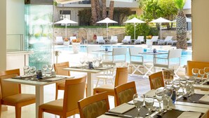 En restaurang med uteservering med utsikt över en pool, utrustad med bord, stolar och parasoller.