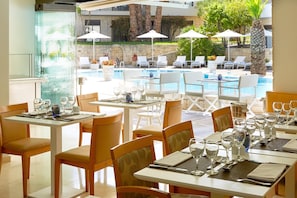 A restaurant with outdoor seating overlooking a pool, equipped with tables, chairs, and umbrellas. - Renaissance Hanioti Resort (Kassandra)
