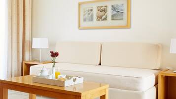 Ein Hotelzimmer mit Holztisch, weißem Sofa, einem gerahmten Bild an der Wand und einem Fenster mit Vorhängen.