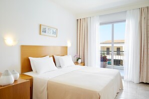 A hotel room with a large bed, two bedside tables, a nightstand, a framed picture on the wall, and a view of the outside balcony.