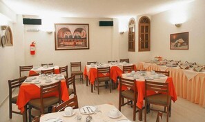 A dining area with round tables set for meals, wooden chairs, and orange tablecloths.