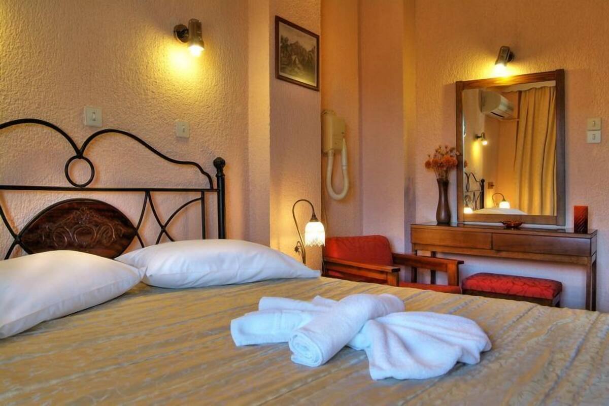 A hotel room with a bed, pillows, a bedside table with a lamp, a mirror, a telephone, and a red chair.