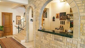 A stone-walled reception area with a staircase, a reception desk, and various framed pictures and decorations. - Olympic Hotel (Delphi)