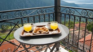 A balcony with a table set for breakfast, including croissants, juice, and coffee. - Olympic Hotel (Delphi)
