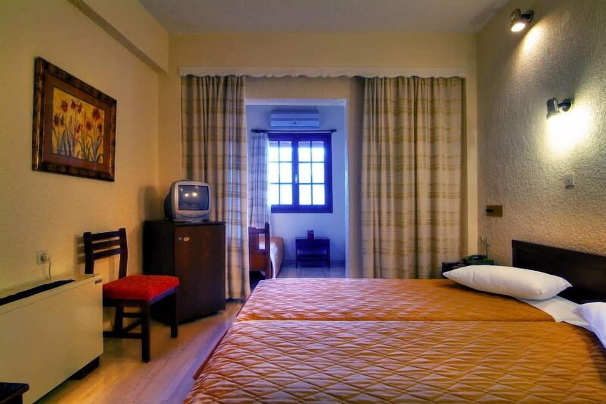 A hotel room with a bed, a desk, a chair, a television, and a window with curtains.