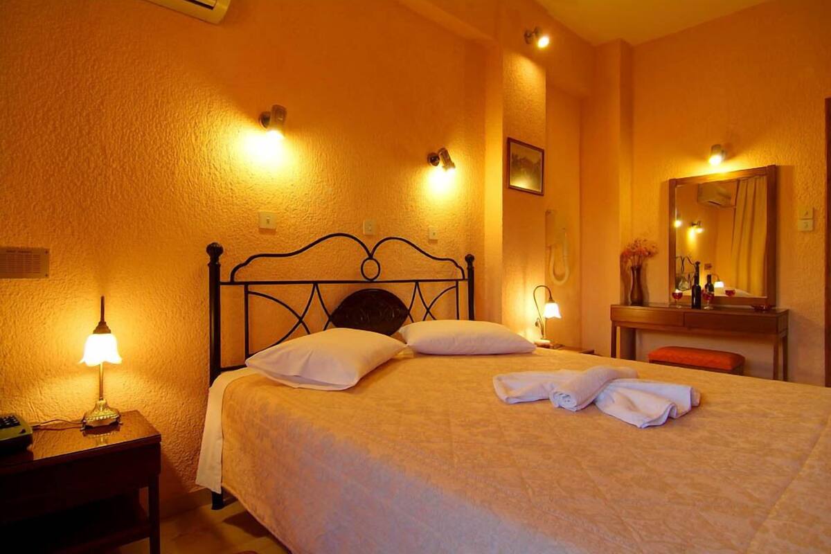 A hotel room with a bed, bedside lamps, a nightstand, a mirror, and a small table with a vase.