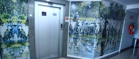 An elevator with a no-smoking sign, a fire extinguisher, and a wall mural of a herd of cattle.