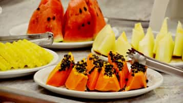 A variety of fruits on plates, including watermelon, pineapple, and papaya, with a pair of tongs on one plate.