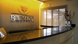 A reception desk with a Brumado Hotel sign, a wooden panel, and a window with blinds. - Brumado Hotel (Campo Grande)