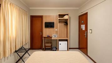 Habitación de hotel con cama, televisión, escritorio con silla, microondas y refrigerador pequeño.