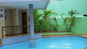 A swimming pool with a water feature, surrounded by plants and a tiled floor. - Brumado Hotel (Campo Grande)