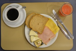 A plate with bread, cheese, ham, butter, a cup of coffee, and a glass of juice on a table. - Brumado Hotel (Campo Grande)