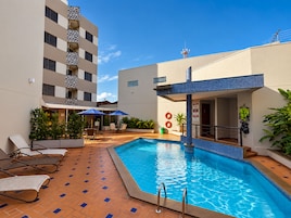 Zona de piscina con sillas de descanso, una terraza con baldosas y un edificio con balcón.