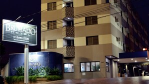 A hotel with a sign reading "BRUMADO HOTEL" and a contact number. The building has multiple floors with balconies and windows. - Brumado Hotel (Campo Grande)