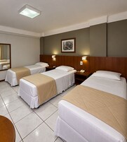 Habitación de hotel con cuatro camas individuales, un espejo grande y un cuadro enmarcado en la pared.