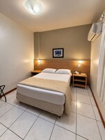 Habitación de hotel con una cama grande, dos mesitas de noche, un aire acondicionado montado en la pared y un cuadro enmarcado.