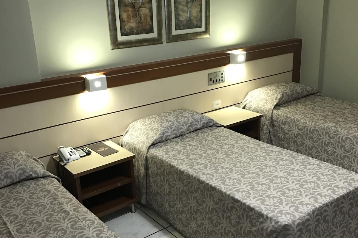 A hotel room with two single beds, a bedside table with a phone and a book, and two wall-mounted lamps.