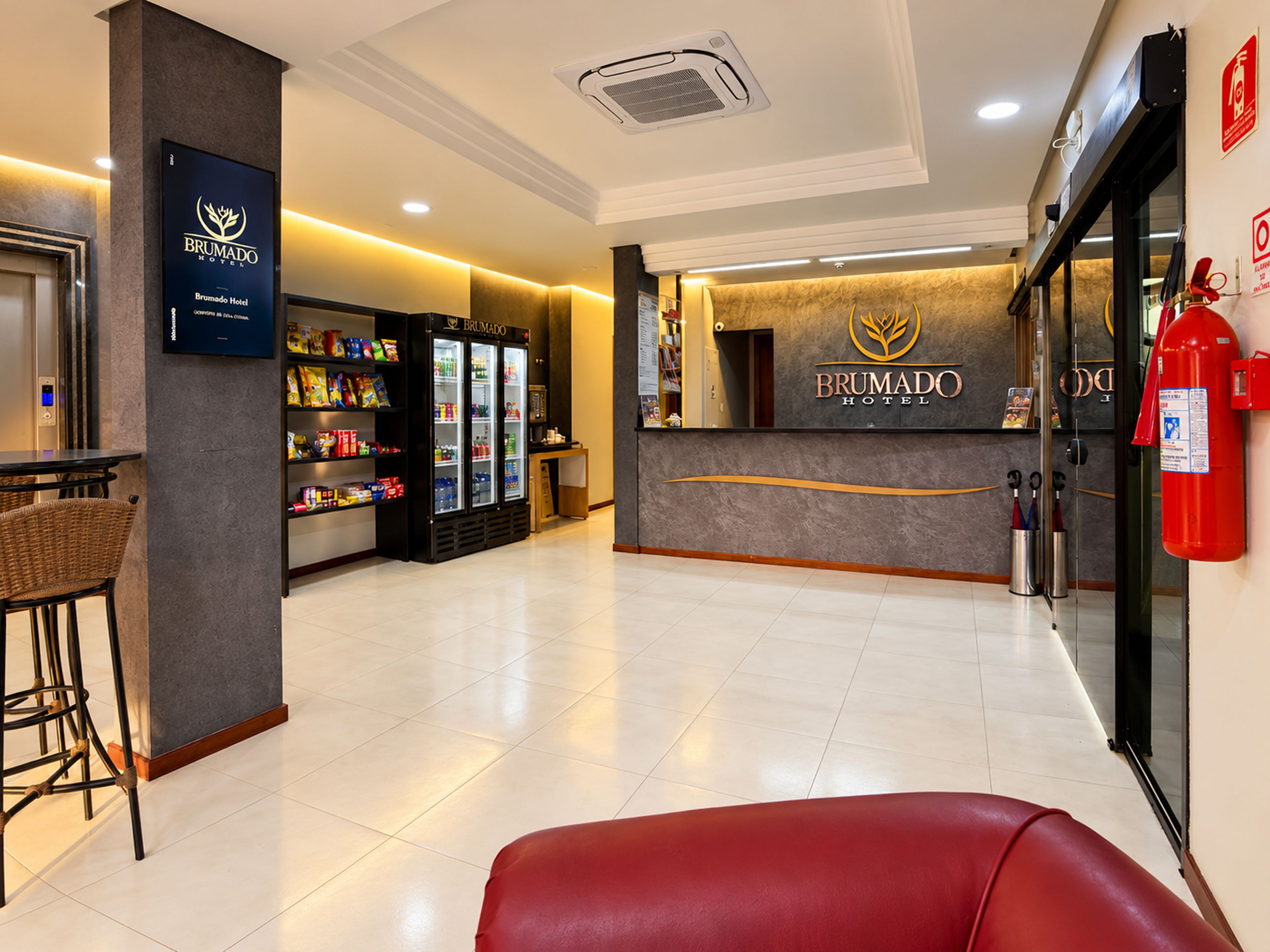 Un espace d’accueil d’hôtel comprenant un comptoir de réception à l’effigie de la marque, un réfrigérateur pour boissons et un extincteur.