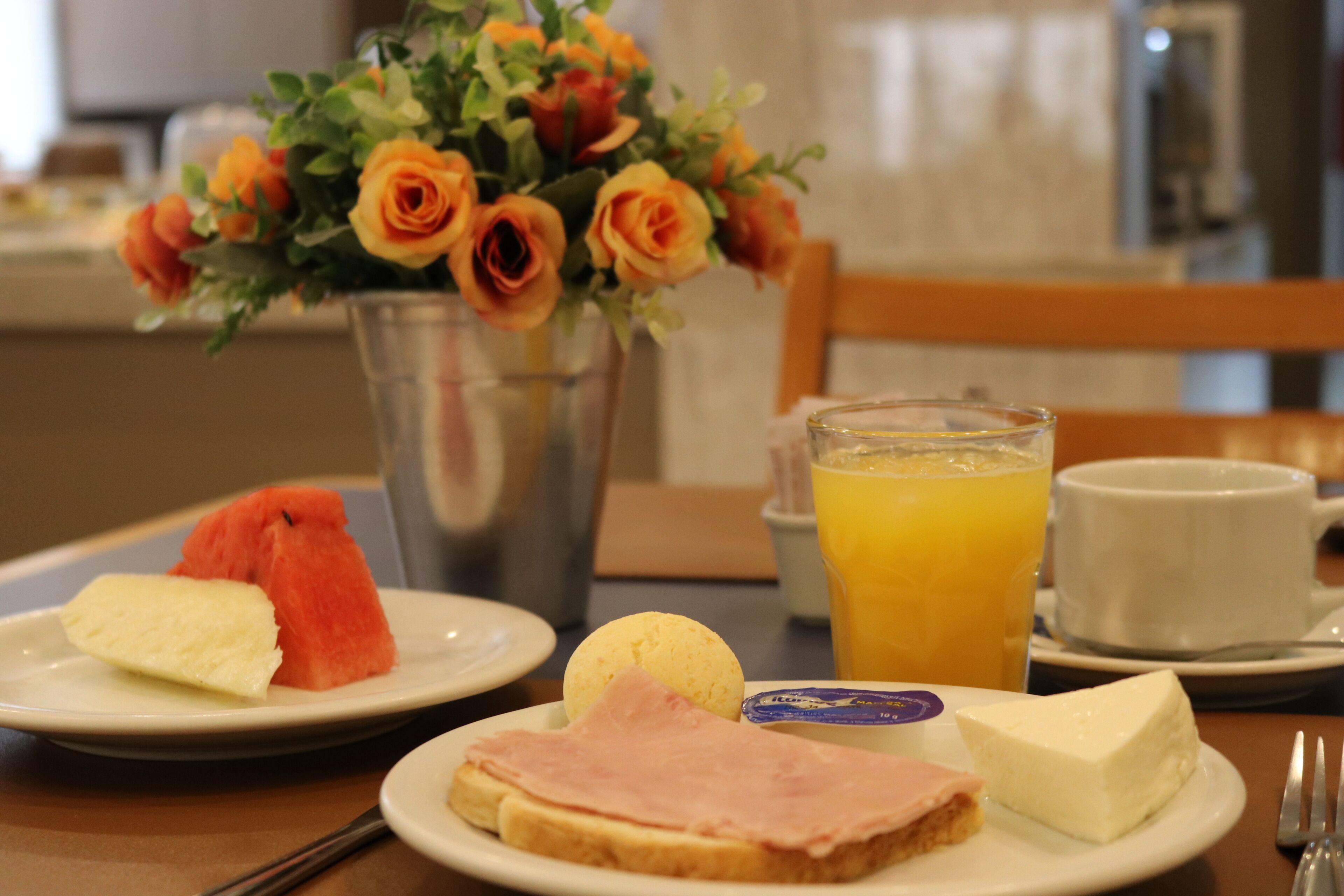 Un desayuno con platos de comida, un jarrón de flores y un vaso de jugo de naranja.