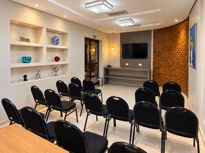A conference room with a long table and chairs, a TV mounted on the wall, and a brick accent wall. - Brumado Hotel (Campo Grande)
