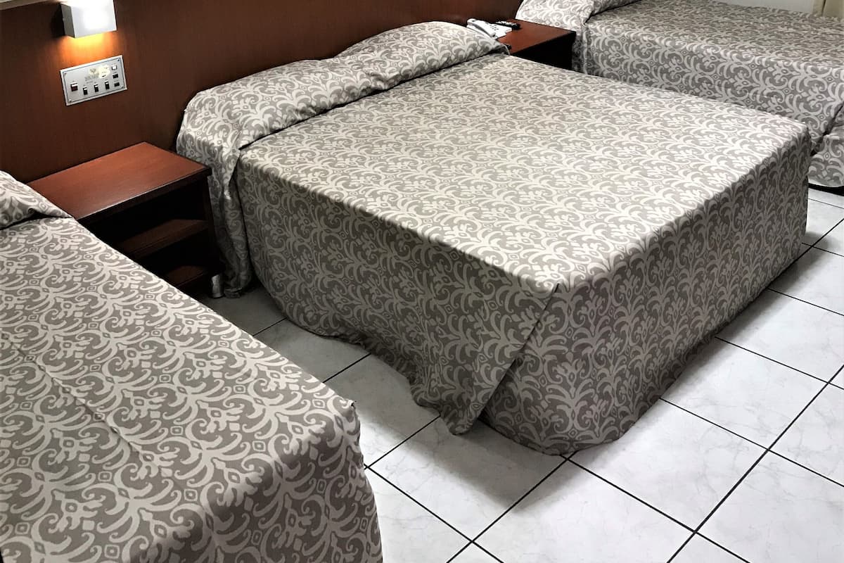 A hotel room with two beds, a nightstand, a wall-mounted air conditioner, and two framed pictures on the wall.