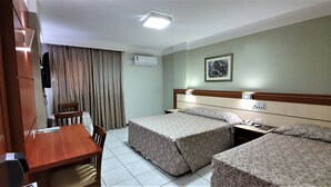 A hotel room with two beds, a desk, a chair, an air conditioner, and a framed picture on the wall. - Brumado Hotel (Campo Grande)